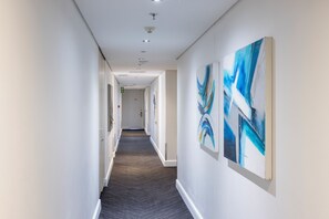A hallway with a carpeted floor, white walls, and ceiling lights. - Newkings Boutique Hotel (Cape Town)