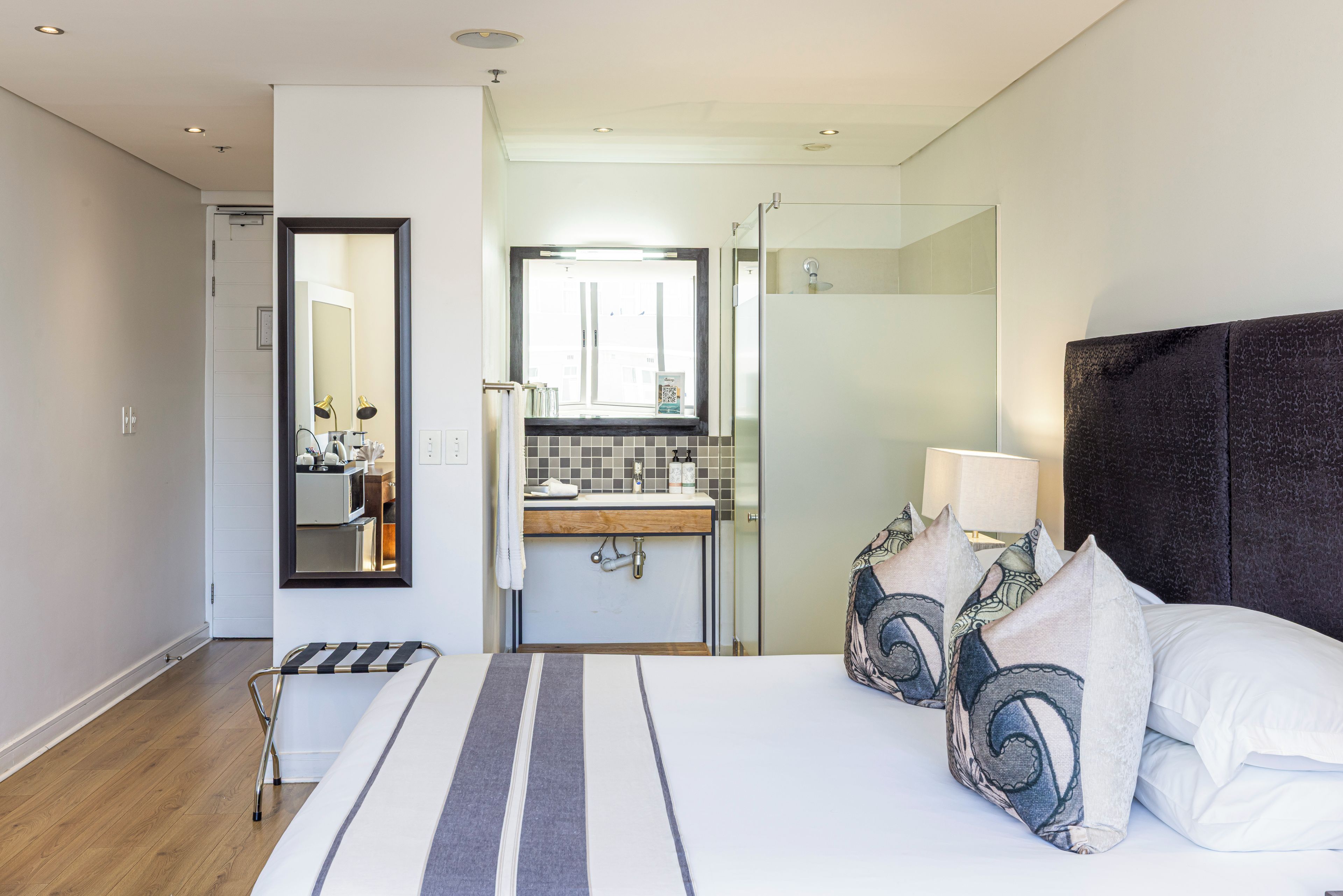 Moderni hotellihuone, jossa on suuri sänky, lasiseinällä varustettu suihku ja näkymä kaupunkiin.