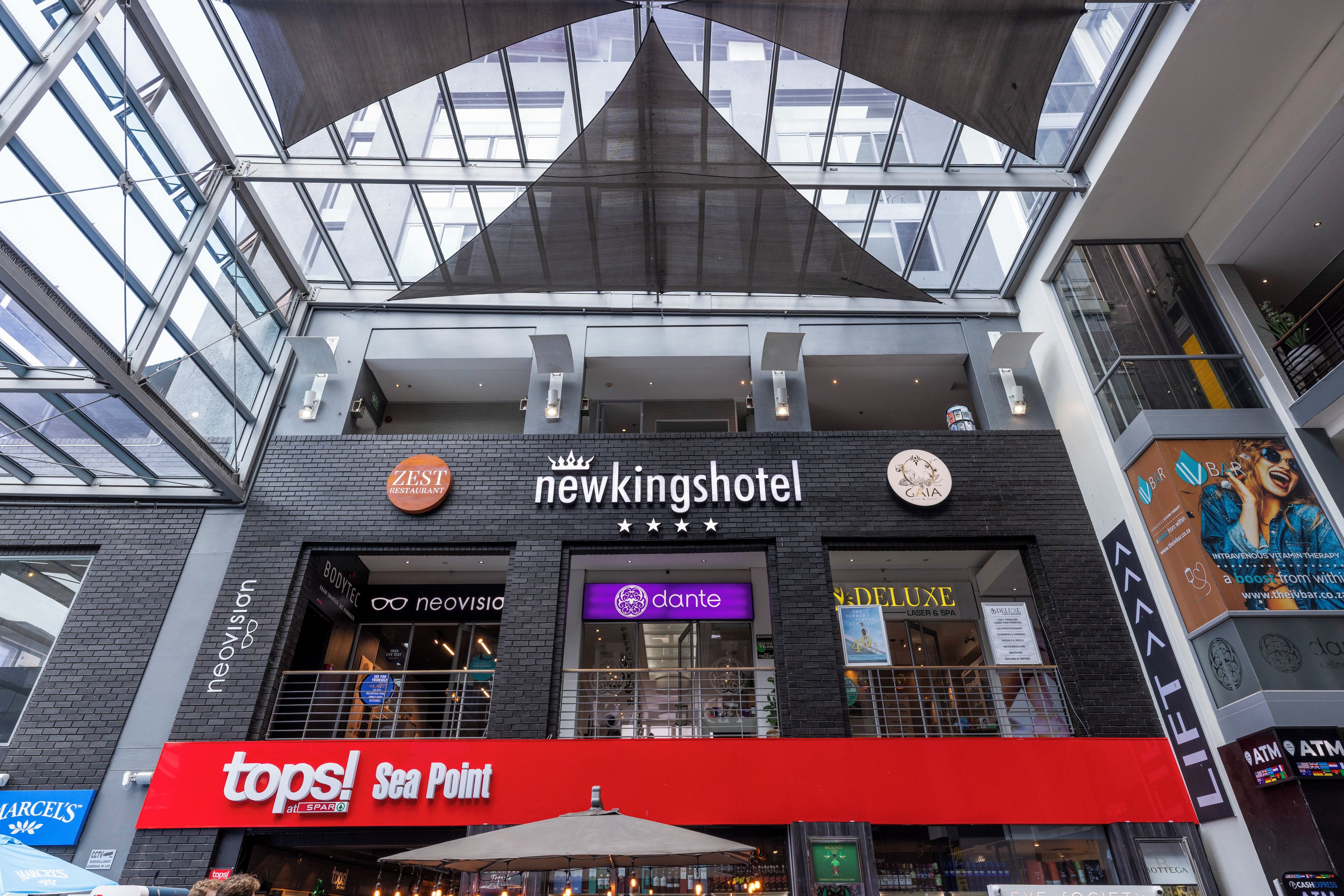 A hotel with a modern architectural design, featuring a prominent sign for 'Newkings Hotel' and various other businesses like 'Topps!' and 'Sea Point' on the ground floor.