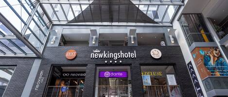 A hotel with a modern architectural design, featuring a prominent sign for 'Newkings Hotel' and various other businesses like 'Topps!' and 'Sea Point' on the ground floor.