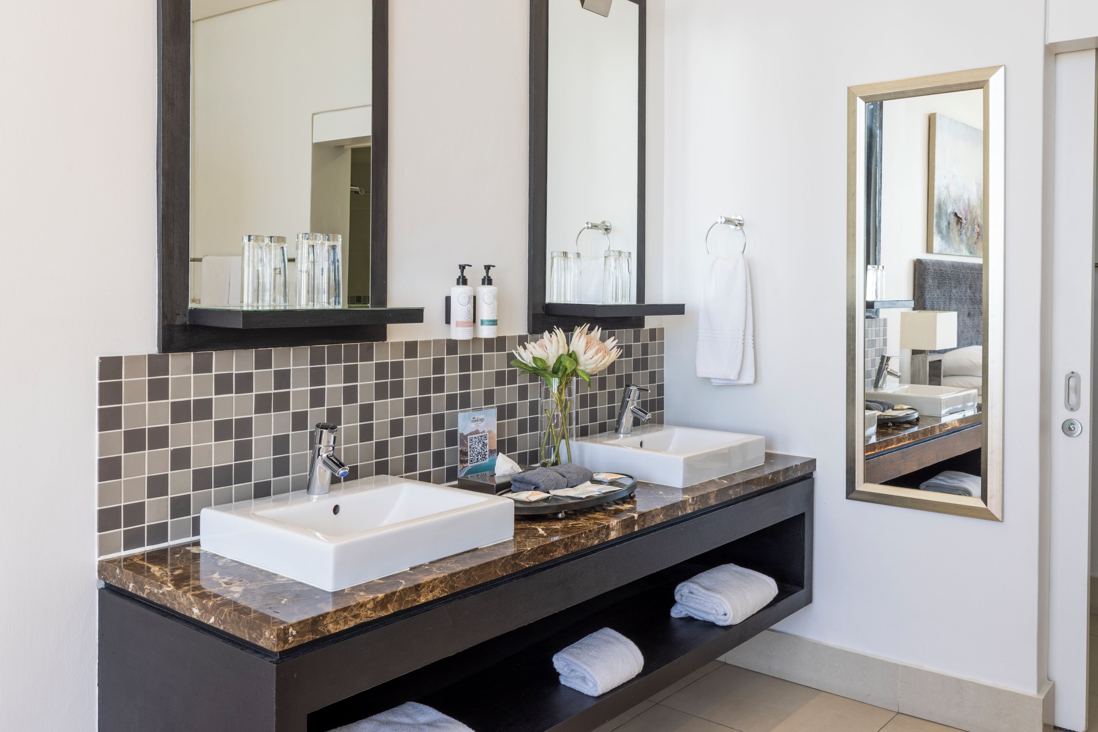 A modern bathroom with two sinks, a large mirror, and a towel rack.