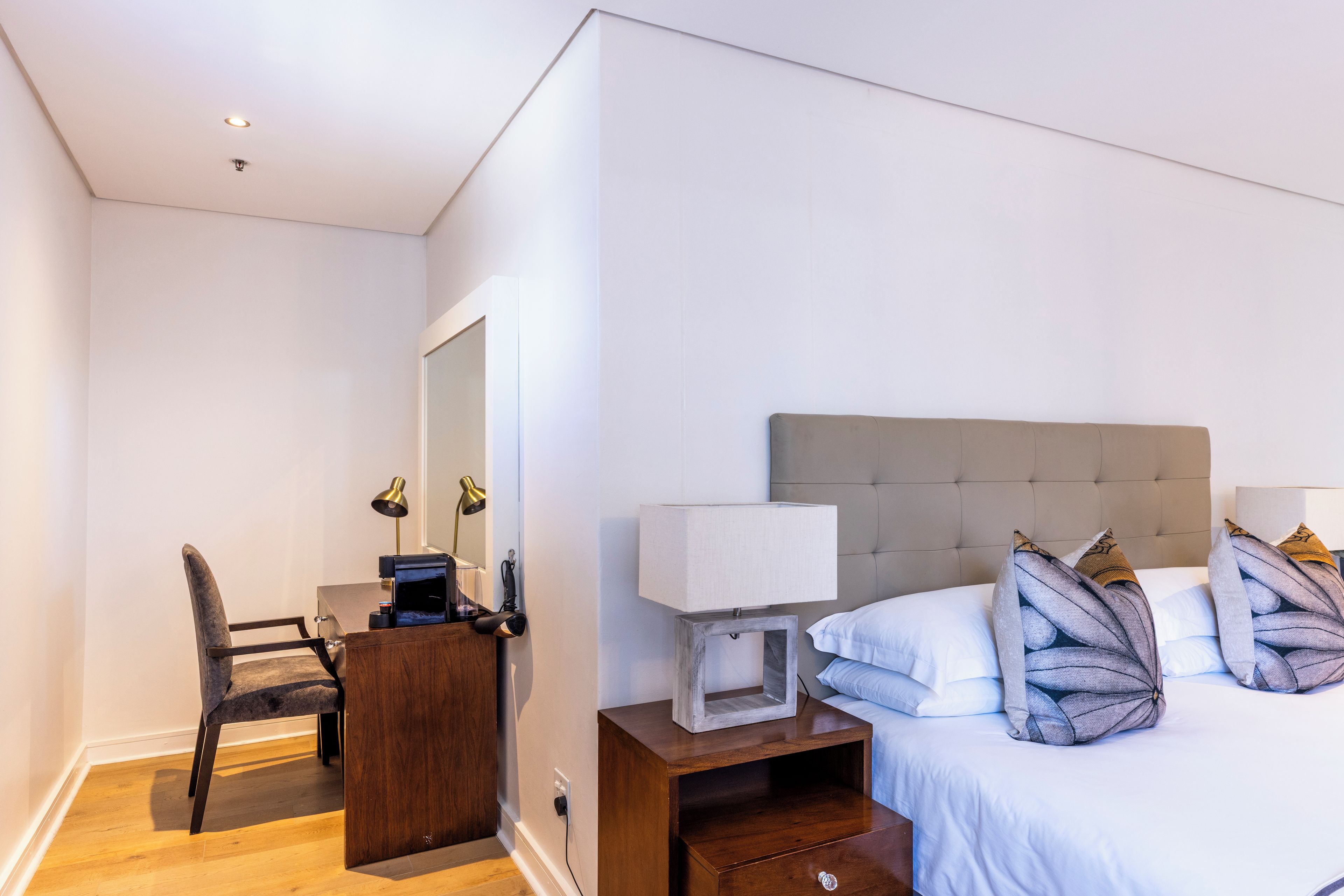 A hotel room with a bed, bedside table, desk, chair, and a mirror.