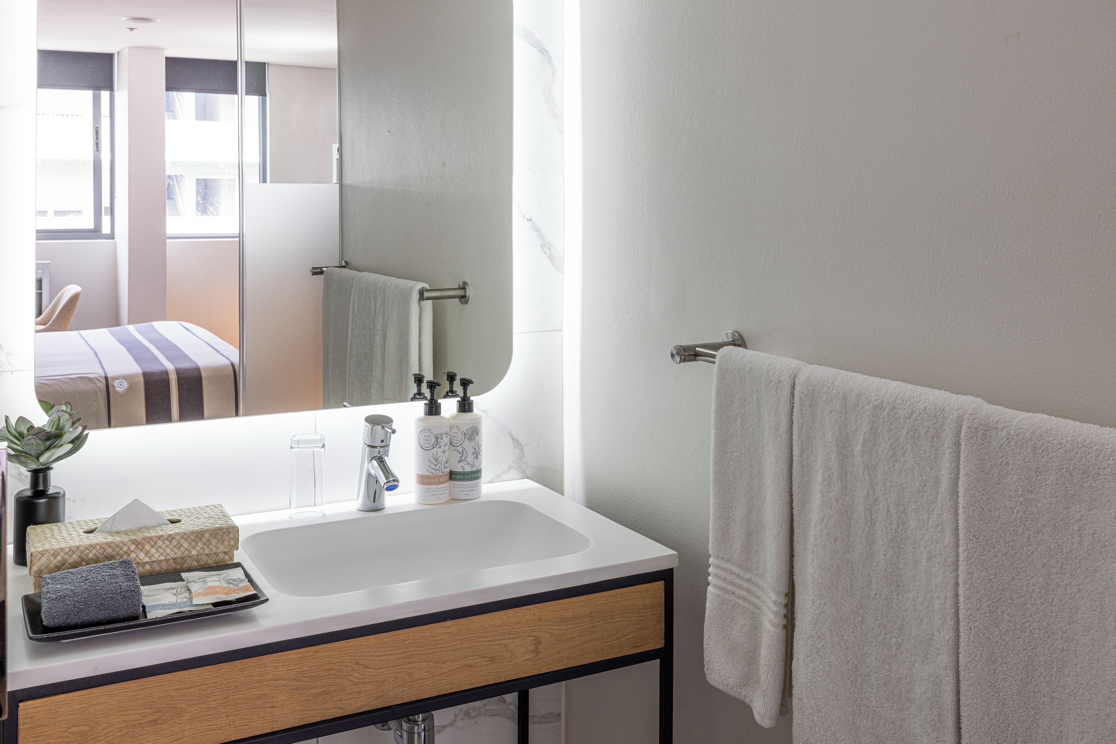 A bathroom with a white sink, a mirror, a towel rack, and toiletries.