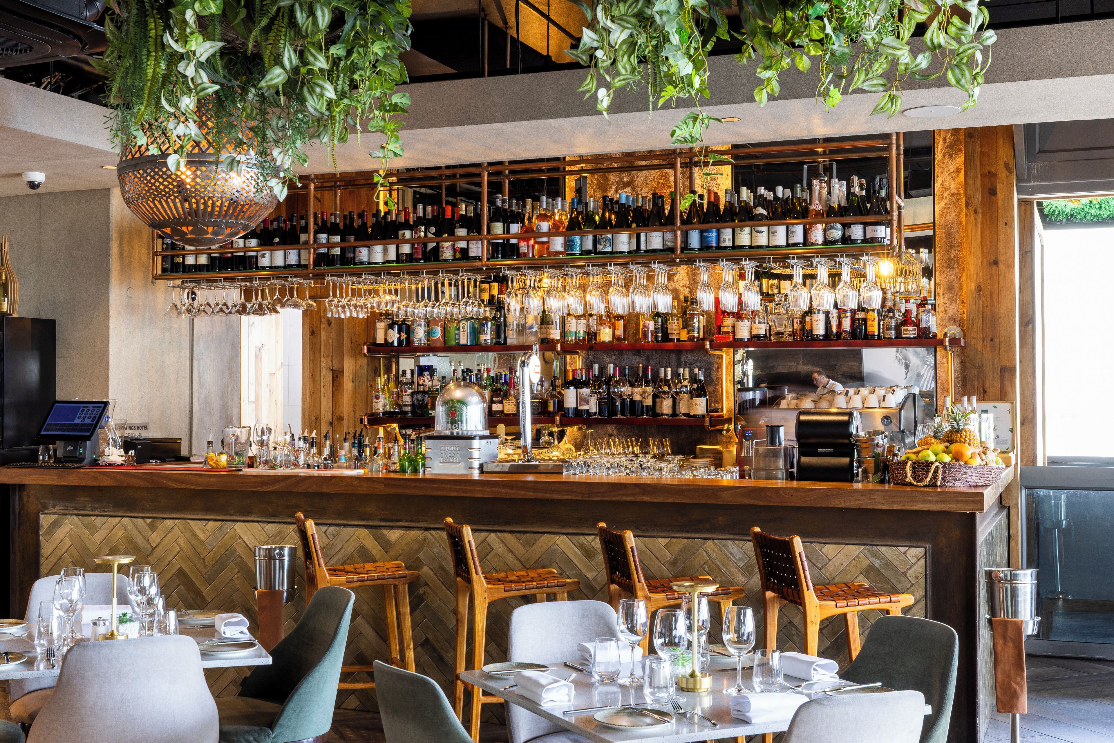 A bar area with a variety of liquor bottles and glasses, a cash register, and a seating area with tables and chairs.