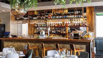 A bar area with a variety of liquor bottles and glasses, a cash register, and a seating area with tables and chairs.