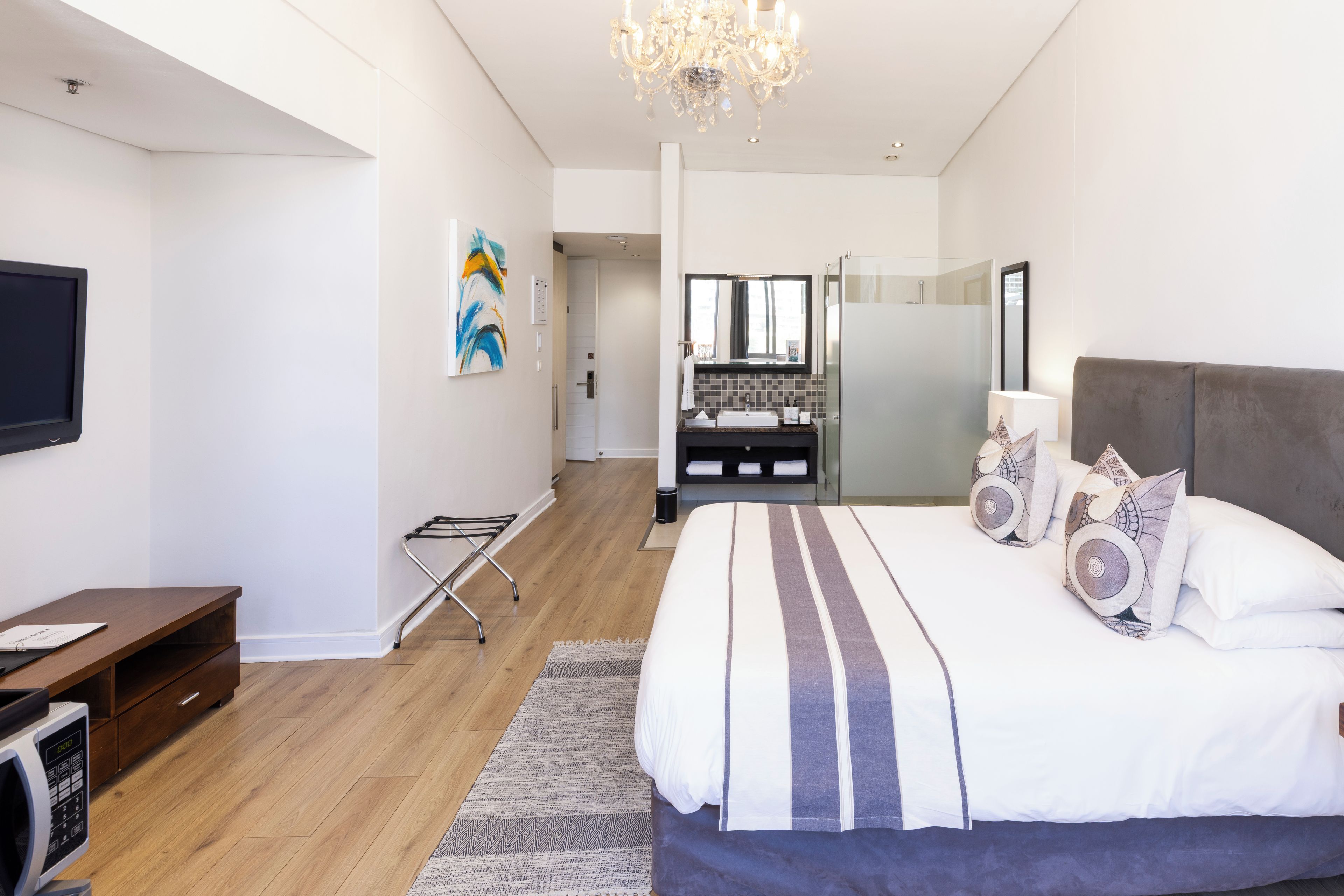 A modern hotel room with a large bed, a flat-screen TV, a desk, and a shower area.