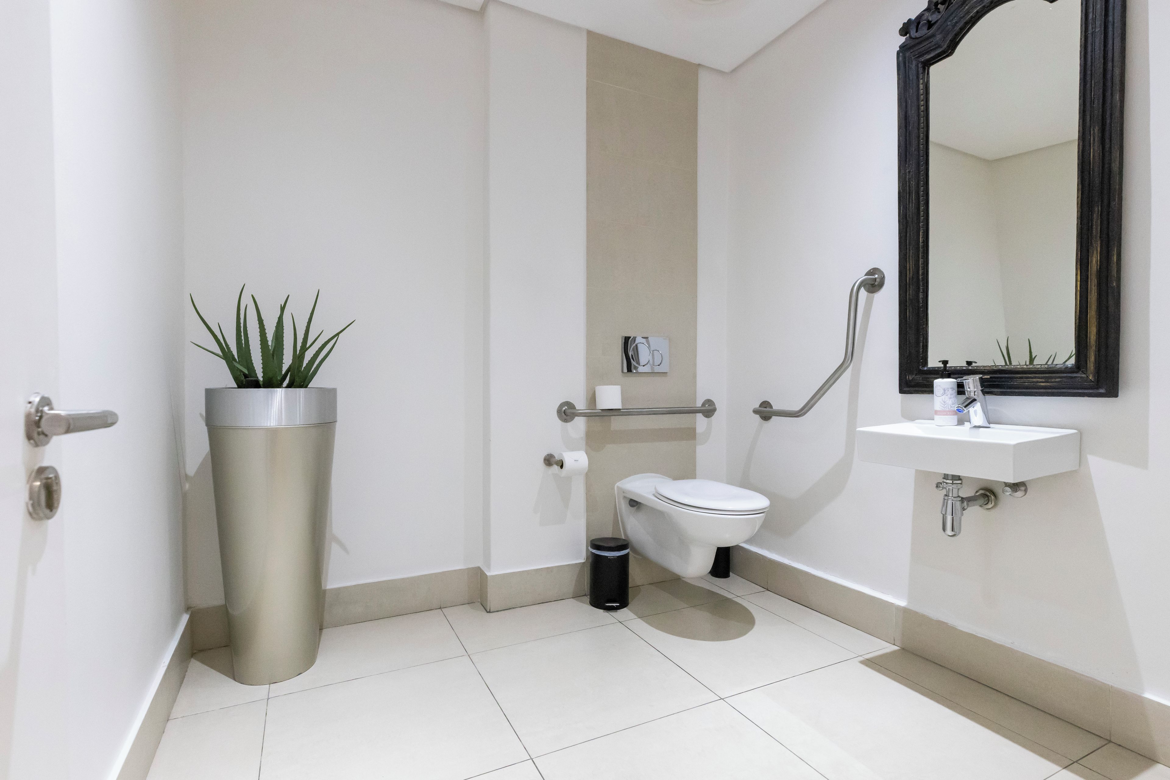 A modern bathroom with a toilet, sink, mirror, and a potted plant.