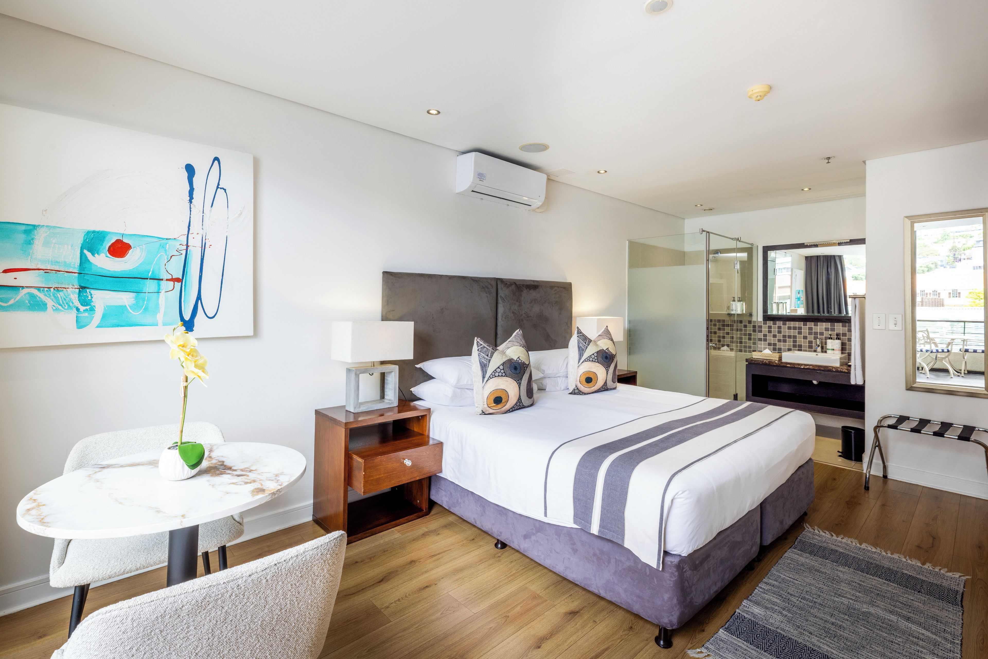 A modern hotel room with a bed, bedside table, lamp, and a painting on the wall.