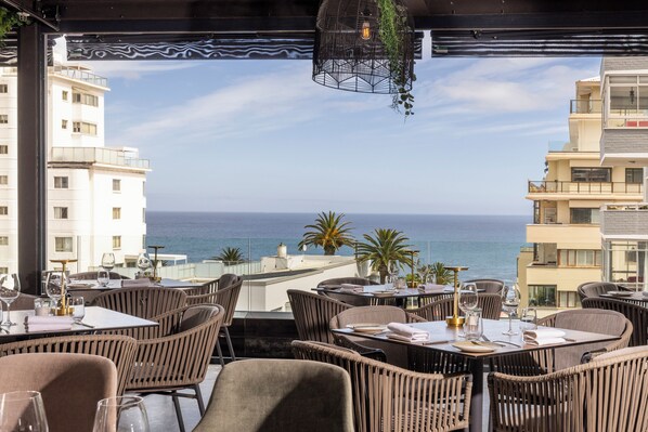 Un restaurante con terraza al aire libre y vistas al mar, con sillas y mesas de mimbre preparadas para comer.