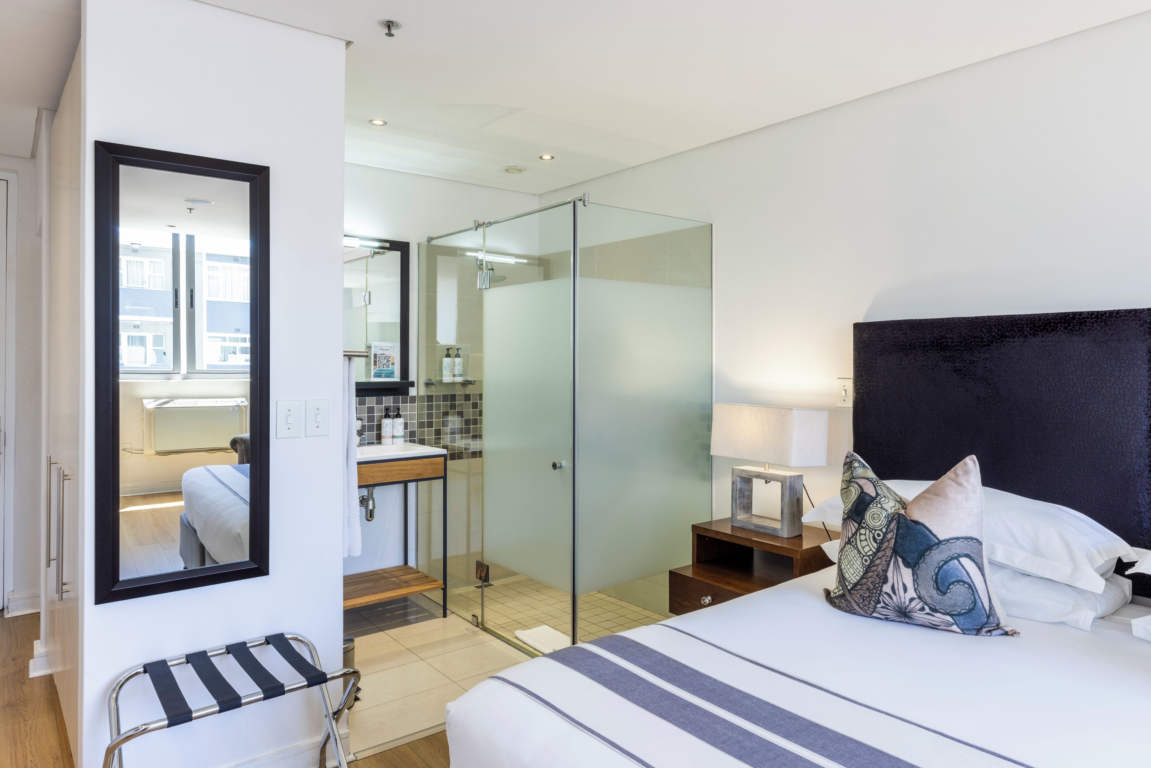 Et moderne hotelværelse med en stor seng, et natbord og et brusebadeområde med glasvægge.