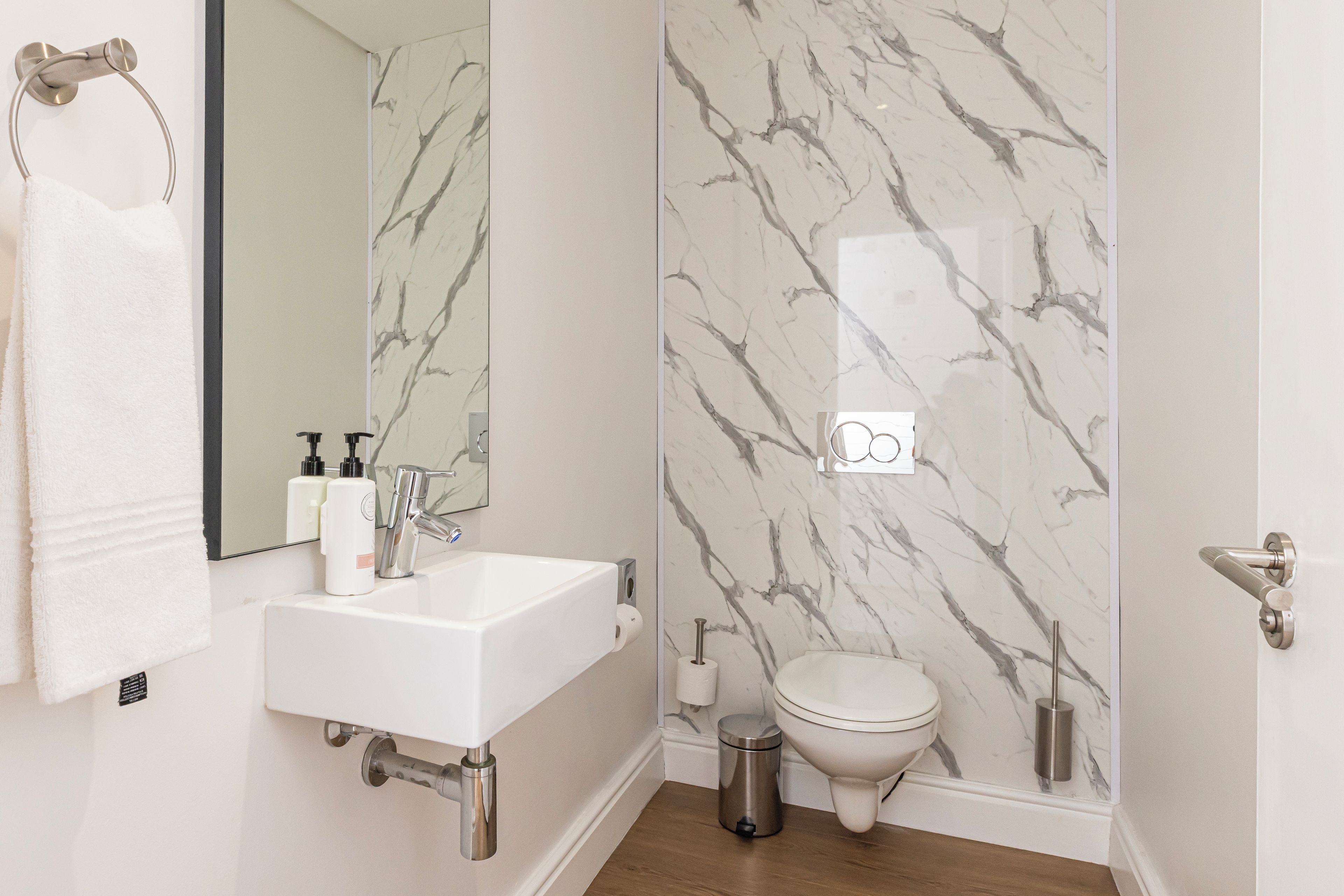 A bathroom with a white sink, mirror, toilet, and marble-patterned walls.