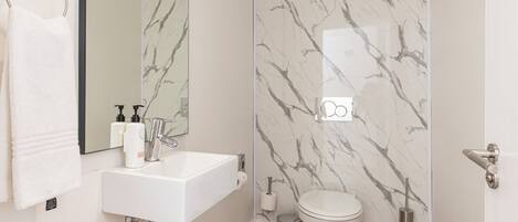 A bathroom with a white sink, mirror, toilet, and marble-patterned walls.