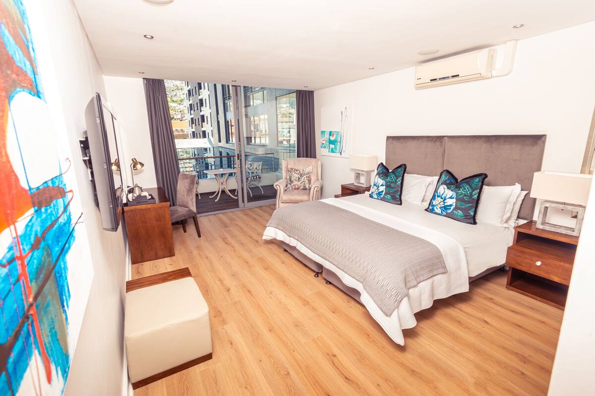 Habitació d'hotel moderna amb un llit gran, una taula de treball, una cadira i vistes a la ciutat a través de grans finestres.