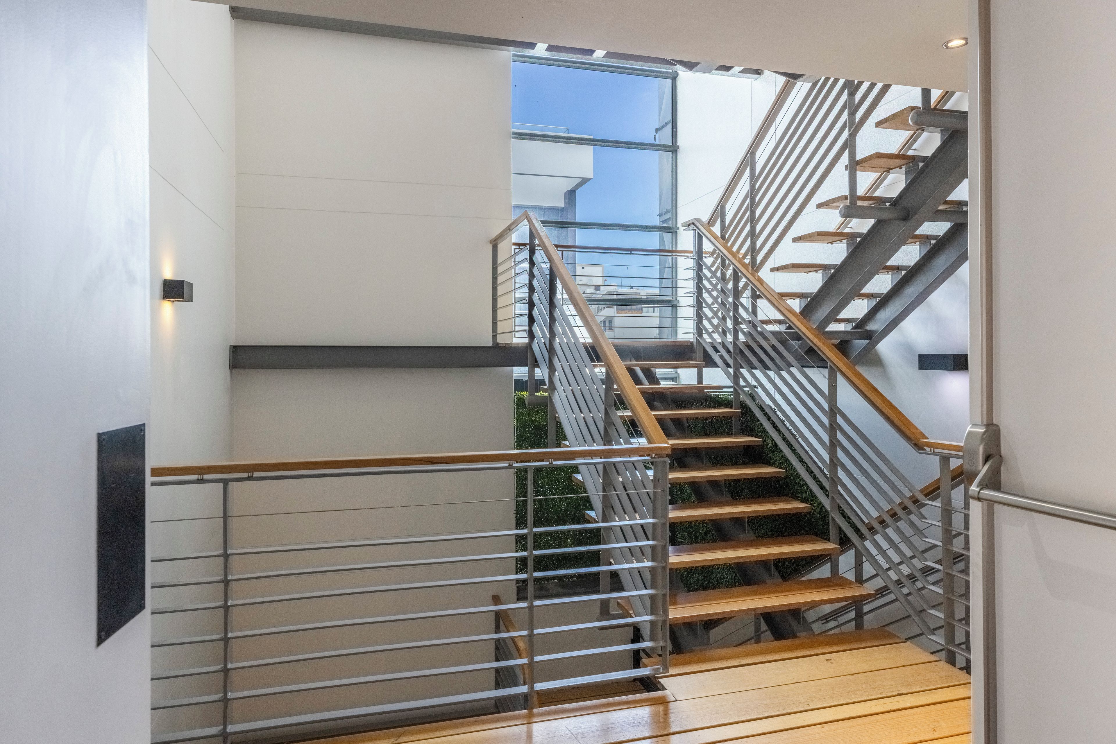 A modern staircase with metal railings and wooden steps, leading to an upper floor.