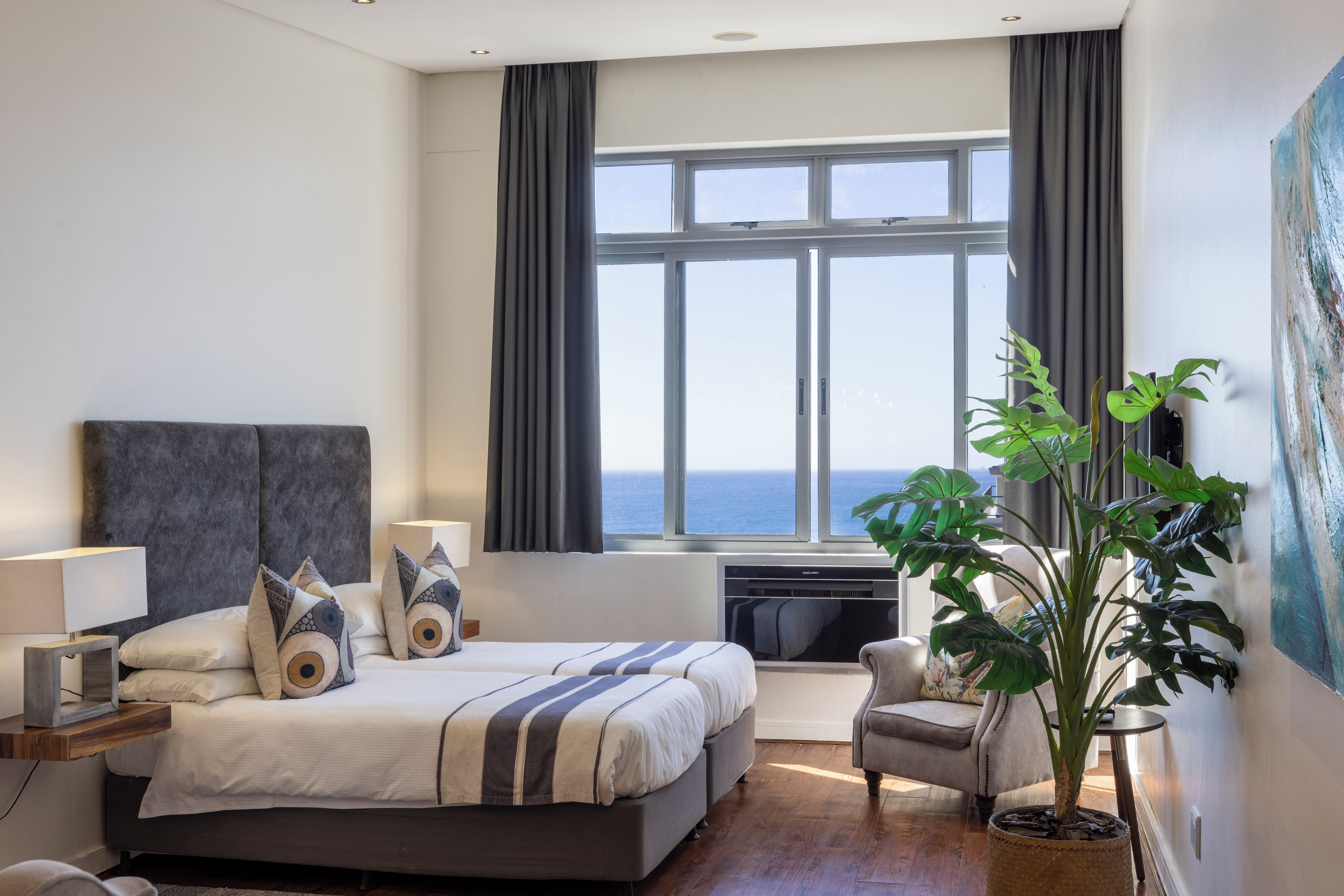 A modern hotel room with a large bed, a desk, a chair, and a view of the sea.
