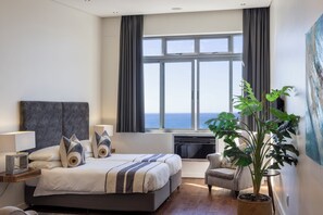A modern hotel room with a large bed, a desk, a chair, and a view of the sea.