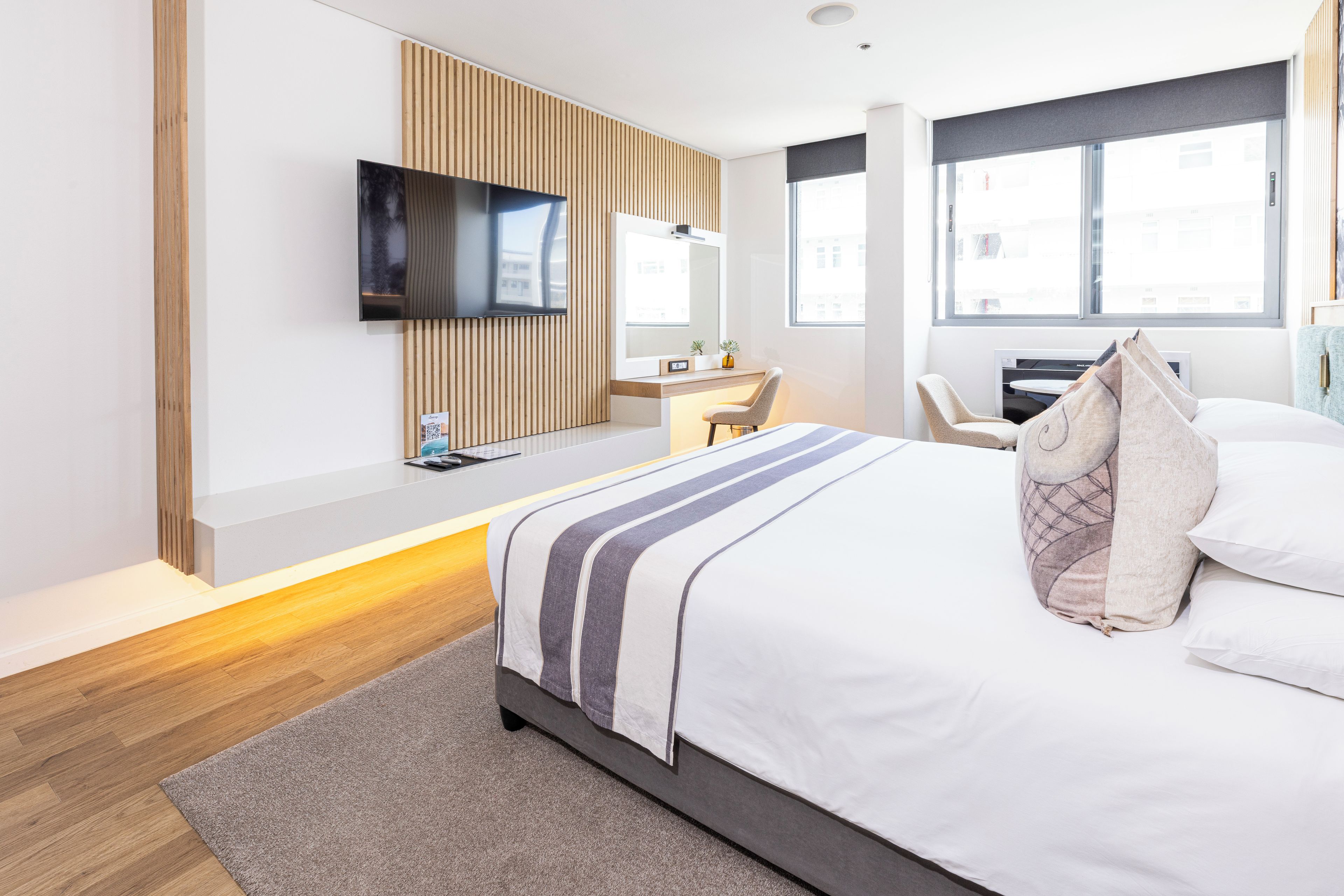 A modern hotel room with a bed, a flat-screen TV, a desk, and a window with a city view.