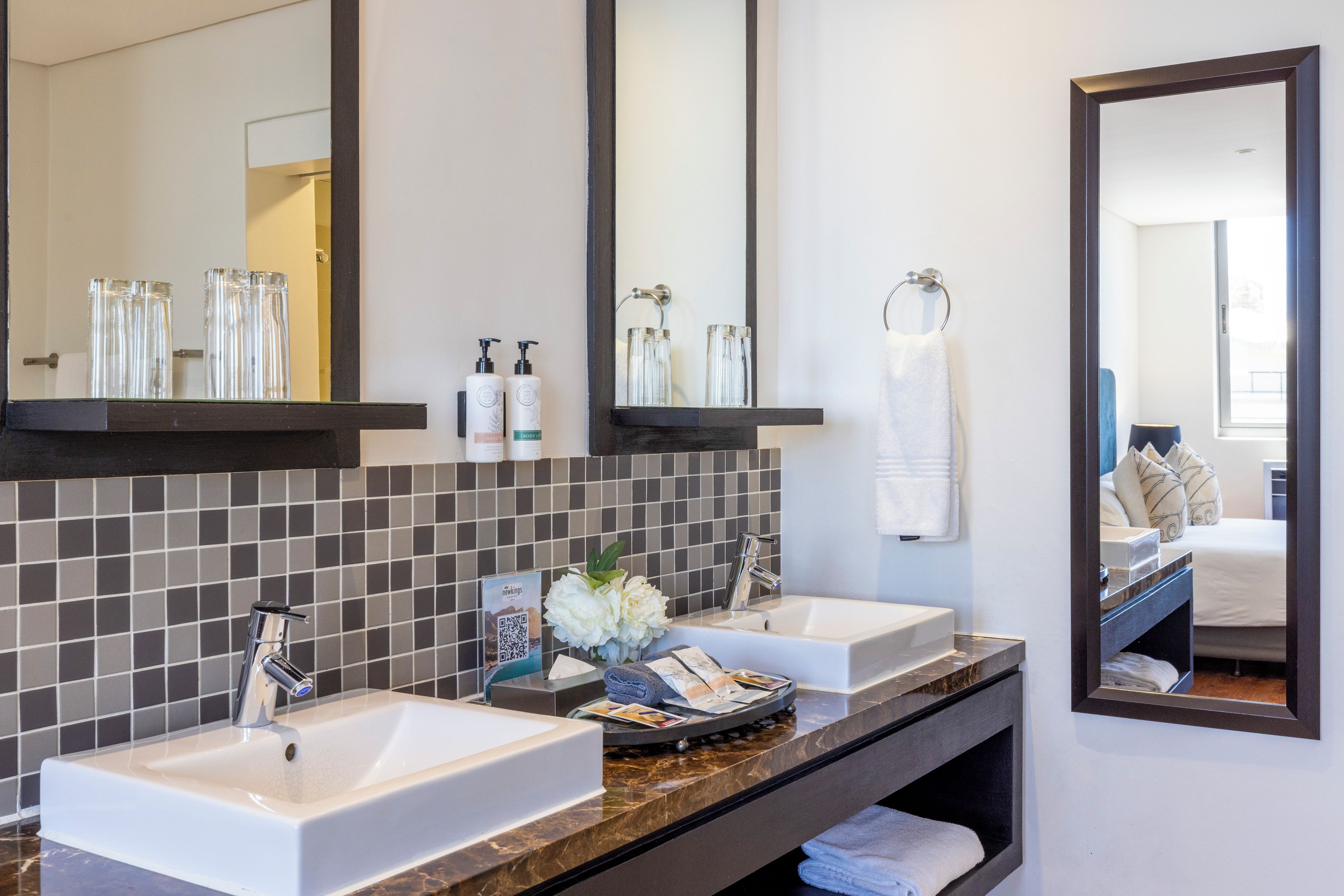 A hotel bathroom with two sinks, a mirror, and a towel rack.