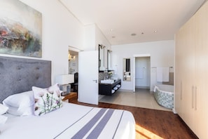 A modern bedroom with a large bed, a bathroom with a bathtub, and a dining area with a chandelier.