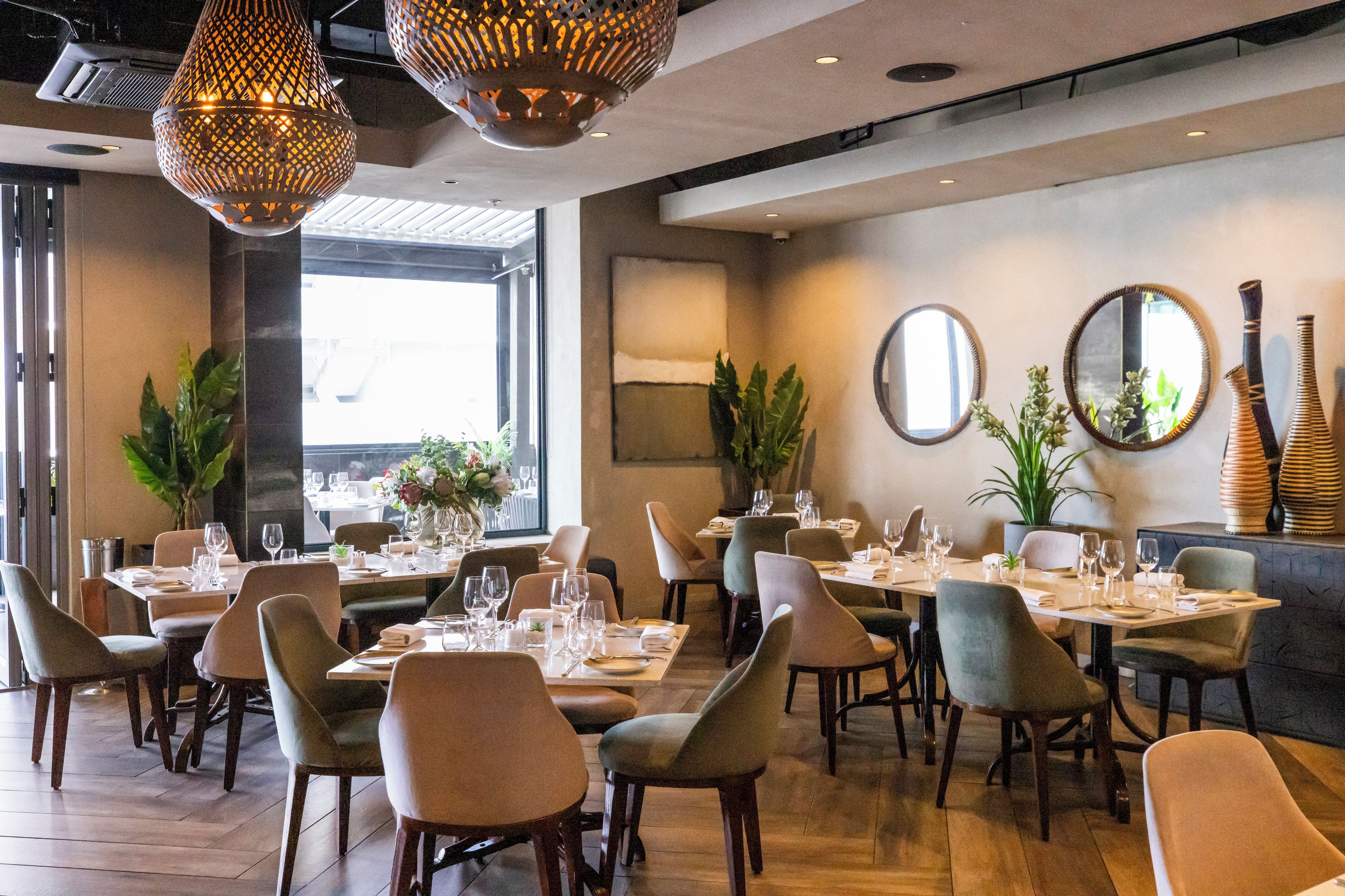 A restaurant interior with multiple dining tables, chairs, and hanging light fixtures.