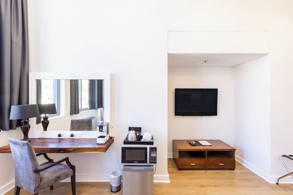 A modern hotel room with a wooden desk, a chair, a microwave, a TV, and a small trash bin.