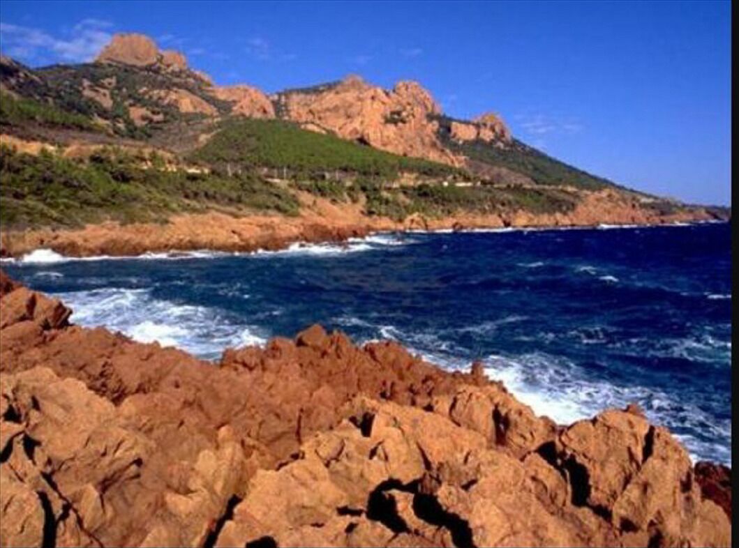 A rocky coastline with waves crashing against the shore and a mountain in the background.