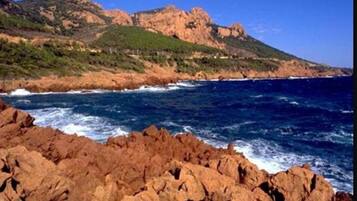 A rocky coastline with waves crashing against the shore and a mountain in the background.