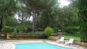 A swimming pool with stone tiles, surrounded by lush greenery and flowering plants. - La Bulle sous les pins (PMR option) (Roquebrune-sur-Argens)