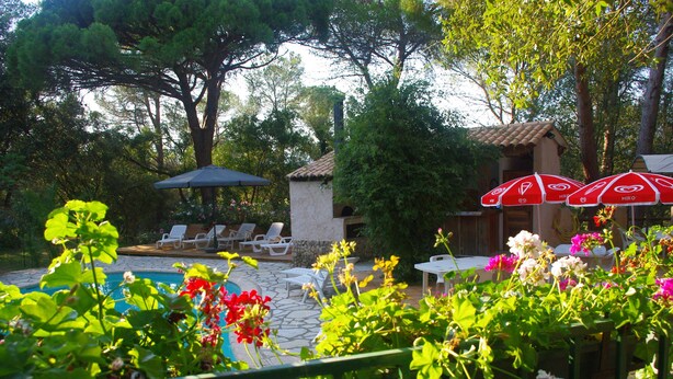 A poolside area with lounge chairs, a small building, and red umbrellas. - La Bulle sous les pins (PMR option) (Roquebrune-sur-Argens)