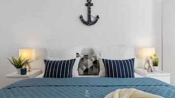 A bedroom with a bed, pillows, bedside tables, a wall-mounted anchor decoration, and a potted plant.