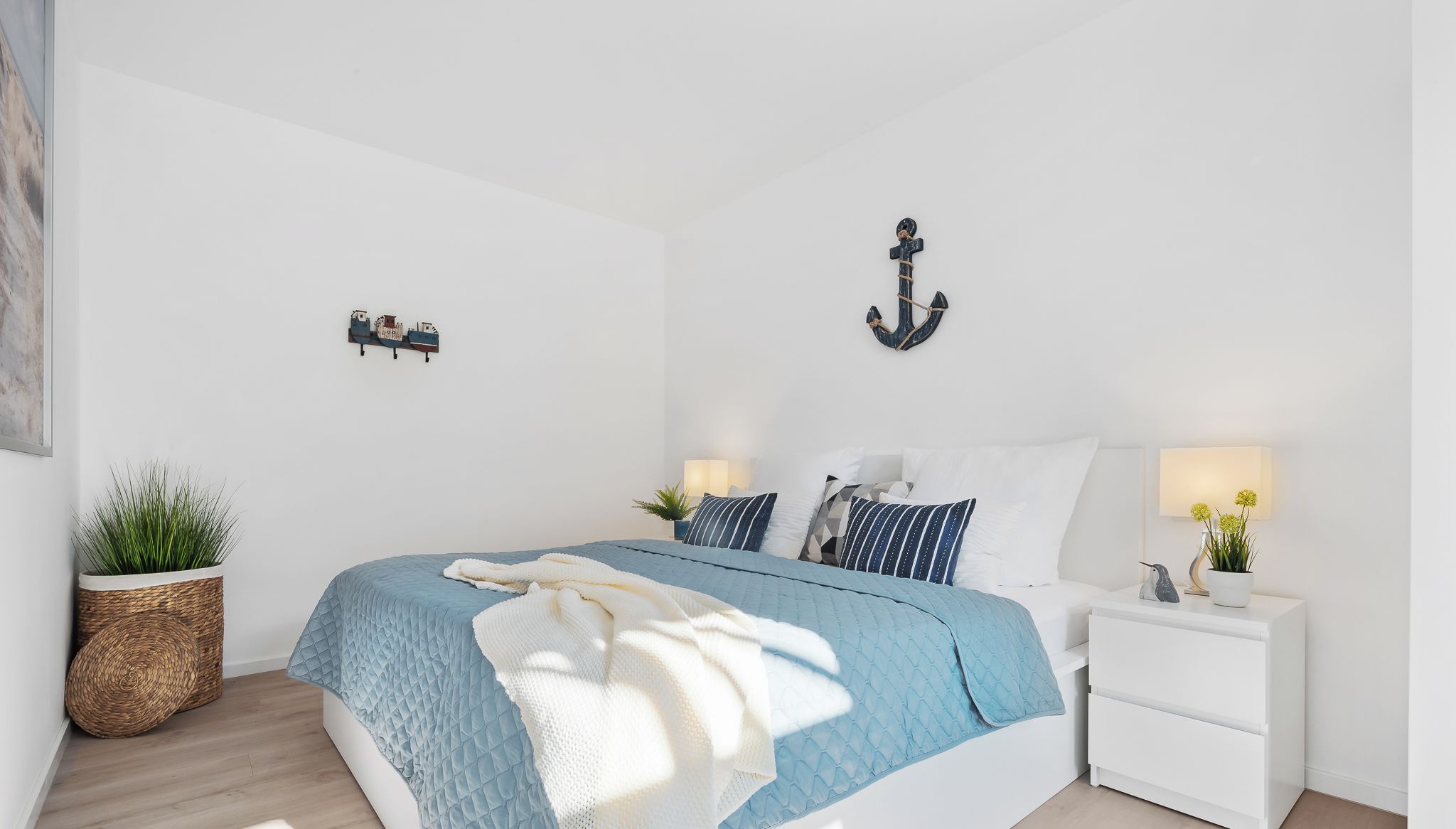 A bedroom with a bed, bedside tables, a wall-mounted light, and a potted plant.