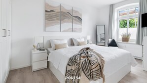 Ein modernes Schlafzimmer mit einem großen Bett, einem Nachttisch, einem Fernseher und einem Fenster mit Vorhängen.