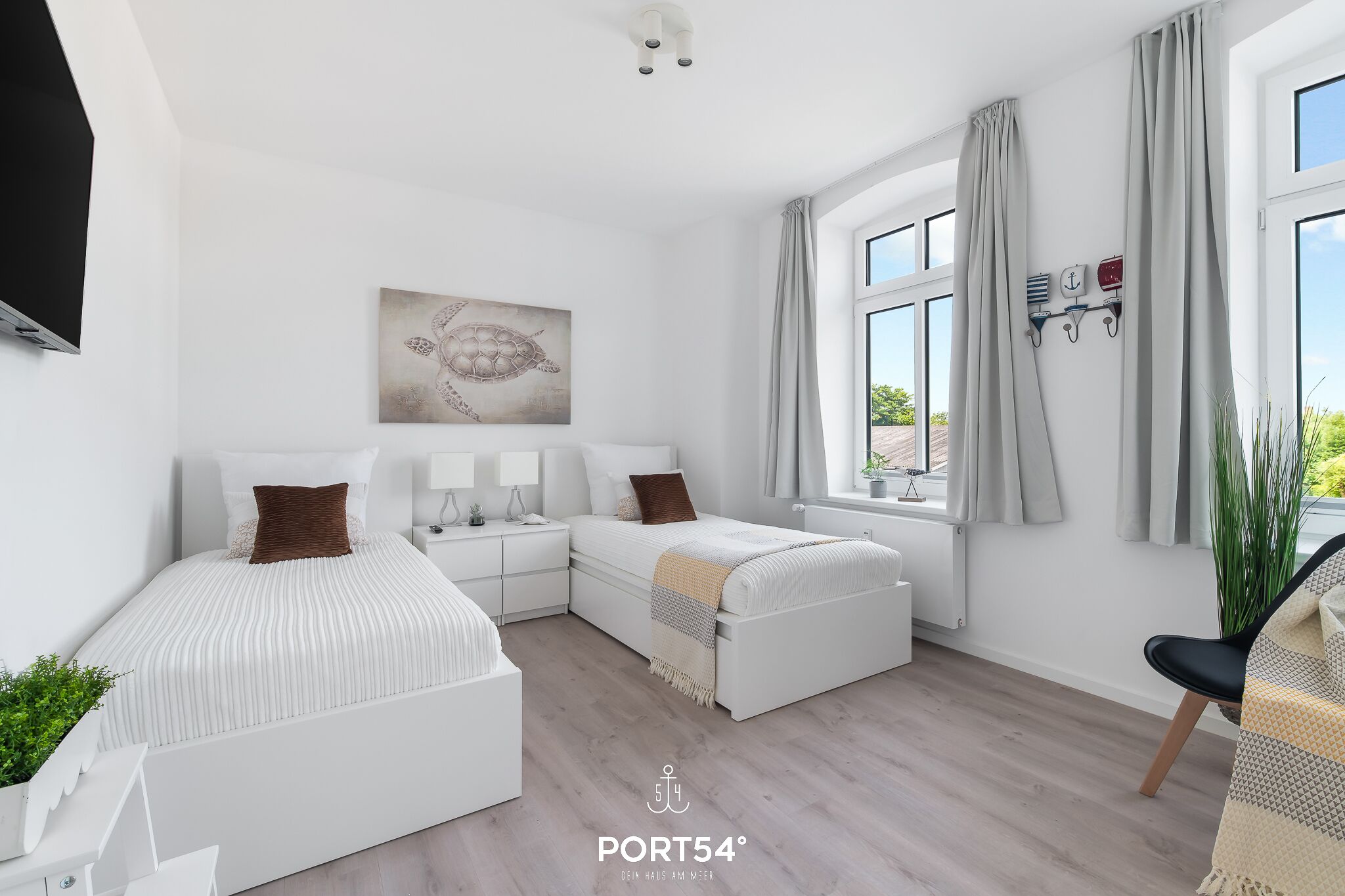 Quarto moderno com cama grande, mesas de cabeceira, TV na parede e janela com cortinas.