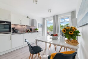 Eine moderne Küche mit weißen Schränken, einem eingebauten Backofen und einem Essbereich mit weißem Tisch und Stühlen.