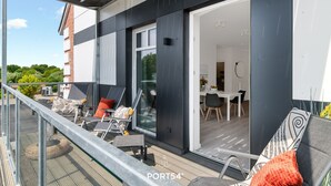Ein moderner Balkon mit Sitzgelegenheit, eine Glastür zu einem Innenbereich mit Essbereich und freie Sicht auf den Himmel.
