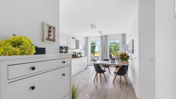 Eine moderne Küche mit weißen Schränken, einem Essbereich mit Tisch und Stühlen und einem großen Fenster für natürliches Licht.