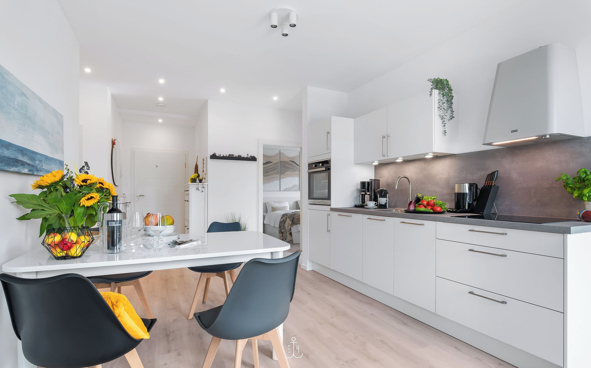 A modern kitchen with white cabinets, a stainless steel range hood, and a dining area with a white table and black chairs.