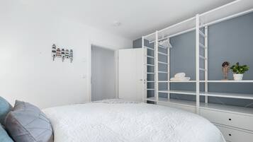 A bedroom with a bed, a white wardrobe with shelves, a small potted plant, and a wall-mounted shelf with towels.