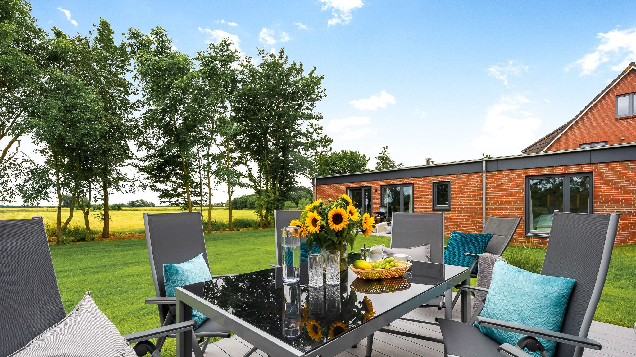 An outdoor patio with a glass table, chairs, and a vase of sunflowers.