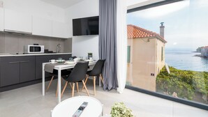 Una cocina moderna con un televisor de pantalla plana, un comedor con mesa y sillas, y un amplio ventanal con vistas al mar.