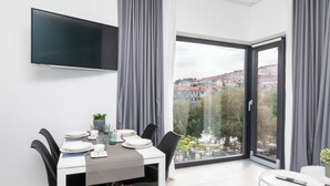 Un comedor moderno con una mesa dispuesta para cuatro personas, un televisor de pantalla plana montado en la pared y un ventanal con vistas a una zona residencial.