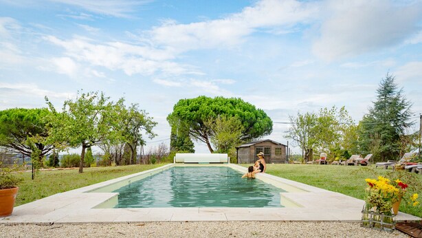 Una piscina rectangular con una cubierta de madera que la rodea, una pequeña construcción de madera al fondo y árboles a ambos lados.