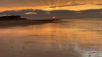 Une plage où l’on peut admirer le coucher de soleil, avec une eau calme et des falaises qui se dressent au loin.