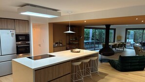A modern kitchen with a central island, bar stools, and a dining area with a large table and chairs. - VILLA CHISTERA with SPA and heated swimming pool (HOSSEGOR)