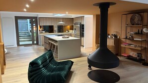 A modern living room with a green sofa, a black fireplace, and a kitchen in the background. - VILLA CHISTERA with SPA and heated swimming pool (HOSSEGOR)