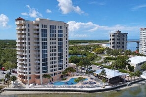 A high-rise hotel with multiple balconies, a swimming pool, and a view of the ocean.
