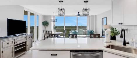 A modern kitchen with a central island, stainless steel dishwasher, and a dining area with a view.
