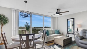 Una sala de estar moderna con comedor, ventanas amplias, ventilador de techo y vistas al exterior.
