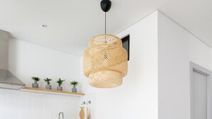 Une cuisine moderne avec des meubles blancs, un îlot central doté de chaises, un luminaire suspendu en rotin et une petite table en bois sur laquelle est posé un objet géométrique.