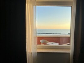 Una finestra vista sull'oceano e un balcone con due sedie e un tavolino.